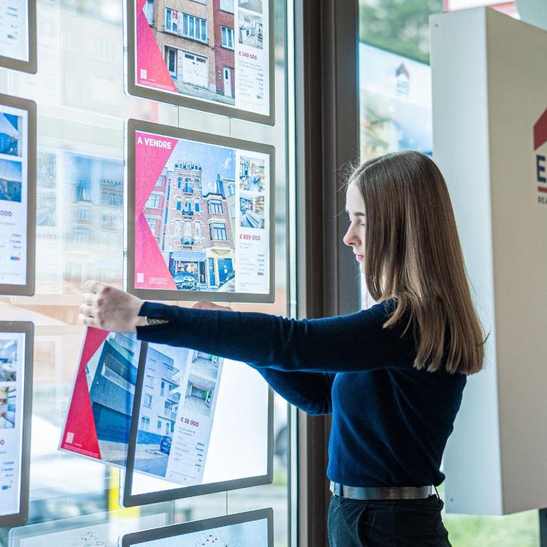 Makelaar hangt fiche in de etalage.