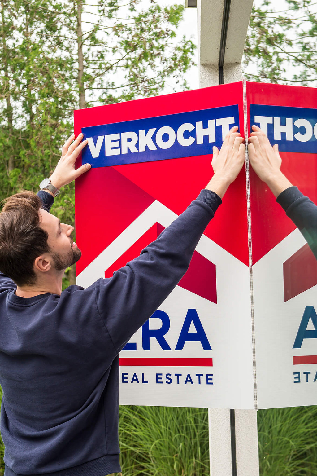 Een man plakt een sticker, met het woord verkocht op, op een verkoopbord.
