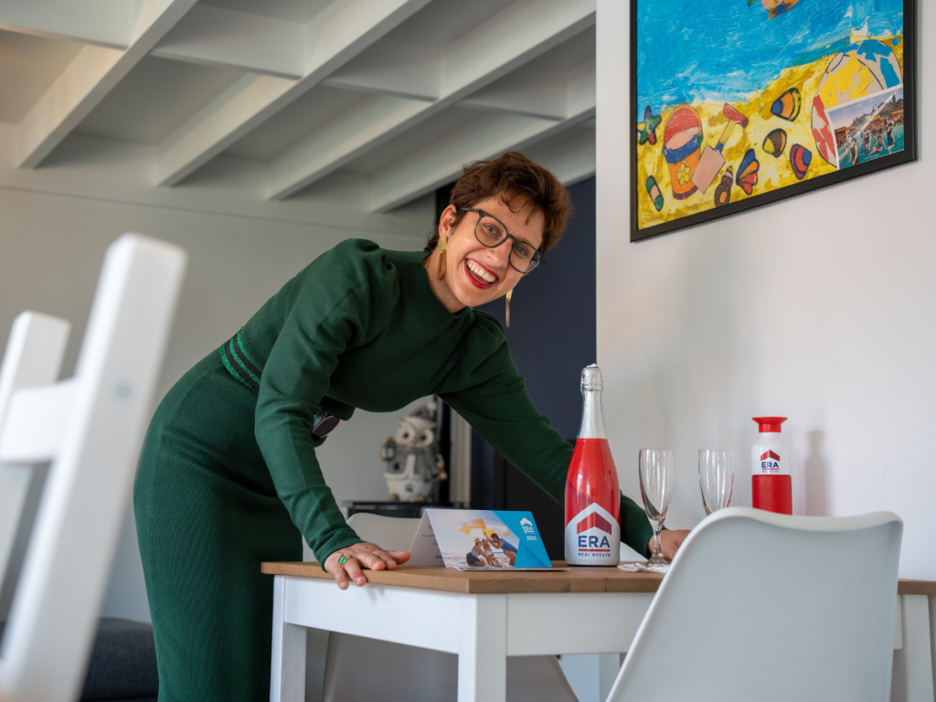 Een lachend makelaar in een pand met een ERA fles, twee champagne glazen en een ERA dopper.